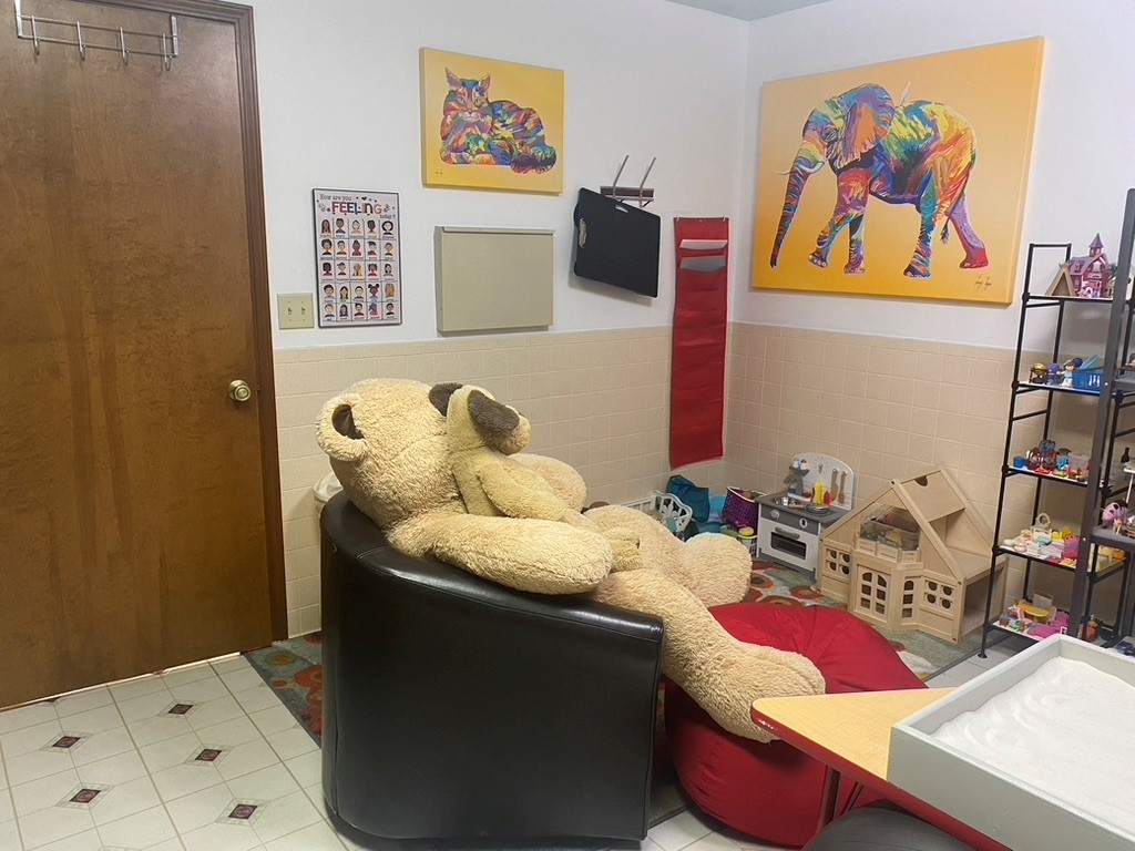 A large teddy bear sitting on a chair in a room with toys